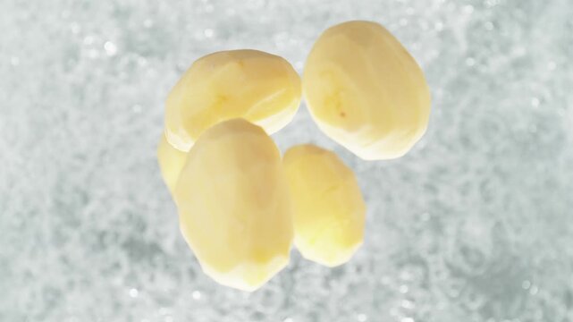 Peeled Potatoes Falling Into Pot Of Boiling Water Making A Splash In Slow Motion, Table Top View