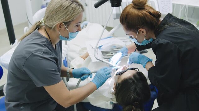 Patient receives dental treatment while lying in a chair at a dental clinic during daytime with focus on tools and dentist's hands