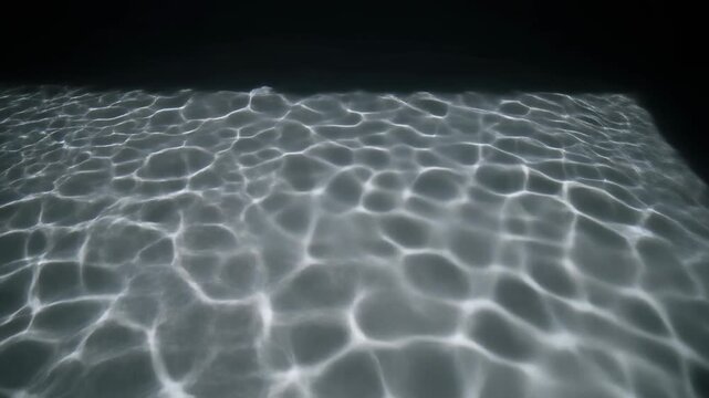 Underwater light reflections create mesmerizing patterns on the bottom of a swimming pool at night.