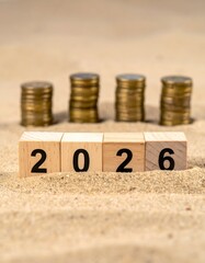 Wooden blocks spelling "2026" with stacks of coins behind on sand