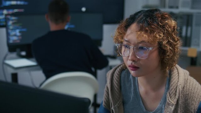 Concentrated Asian Female Software Developer, Programmer using Desktop computer, Writing code, Developing Software Working on Ai Machine learning project sits at office desk in tech office at night.