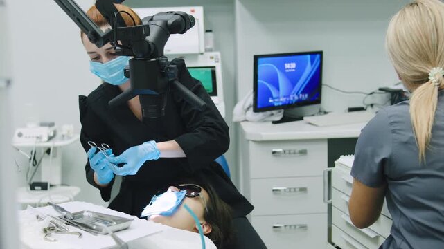 Dentist and assistant work together in dental clinic providing treatment to patient during checkup while maintaining safety protocols