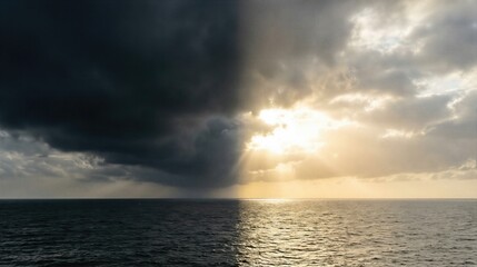 Obraz premium Dividing sky showing dark storm clouds over a calm sea on one side and a bright sunlit sky over sparkling water on the other. Creation of light and dark.
