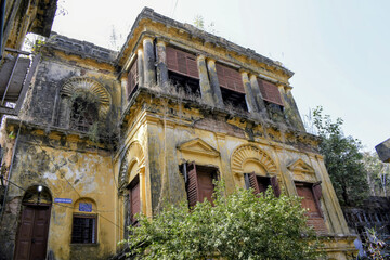 historic narajole rajbari mansion facade with ornate arches peeling plaster weathered walls vegetation growth and colonial architectural details reflecting abandoned aristocratic heritage