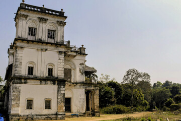 facade construction shows weathered twin corinthian columns with acanthus capitals, sunburst relief motifs, and wooden louvered shutters set in decaying masonry