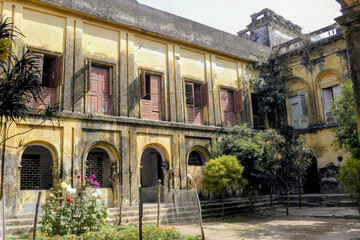 Fototapeta premium wide view of the weathered yellow inner courtyard of narajole rajbari, featuring arched doorways, old wooden shutters, and a central garden under bright daylight