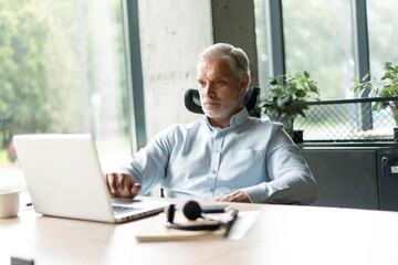 Happy mature European business man ceo trader using computer, typing, working in modern office