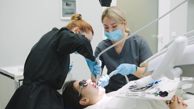 Two dental workers examine a patient during a checkup in a dental clinic. One worker uses tools while the other assists with the treatment process.