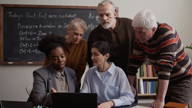 Black female teacher working together with four Caucasian senior students on laptop and sharing interactive discussion during lesson in modern classroom learning environment
