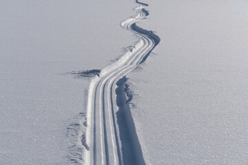 A sled trail stretching into the distance on fresh loose snow