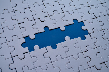 Fototapeta premium White jigsaw puzzle pieces surround a missing center piece revealing blue