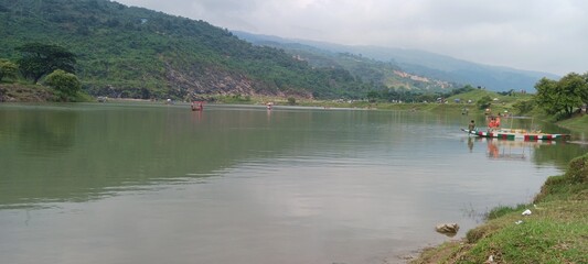 A beautiful summer landscape featuring a scenic mountain lake with green forest reflections under a blue sky and white clouds