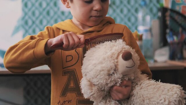 Boy brushing a white teddy bear with a hairbrush - Heartwarming 4k footage of imaginative play and nurturing as a young child cares for a stuffed animal
