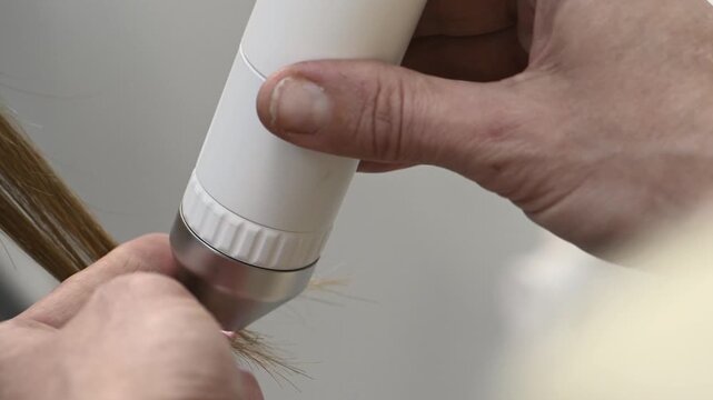 Trichologist examines hair and scalp of young woman in salon using trichoscope and dermatoscope. Hair loss, split ends problems, scalp treatment and hair care consultations Closeup hands no face