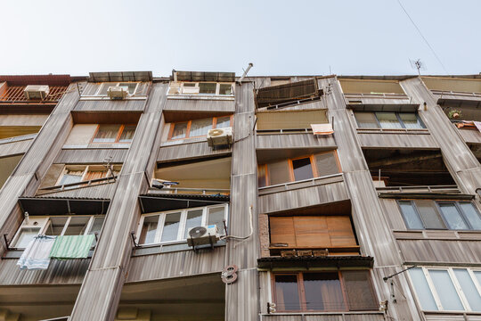 View of a worn, grey building with jutting balconies, air conditioning units, and open windows showing domestic life, Yerevan, Yerevan, Armenia.