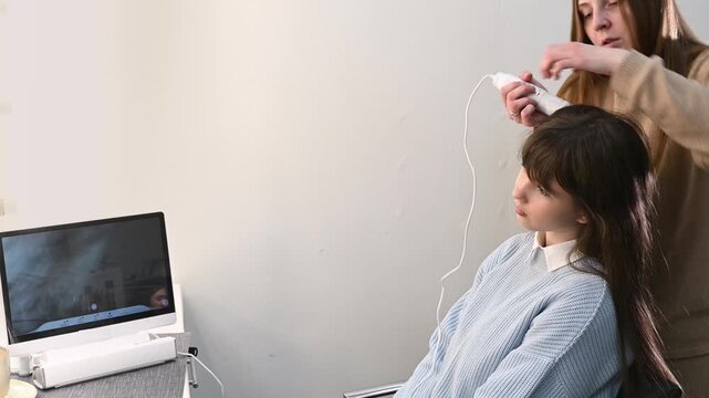 Trichologist examining scalp with digital dermatoscope, close up of hair and skin analysis on screen. Woman specialist performing hair diagnostics procedure in modern clinic, medical consultation conc