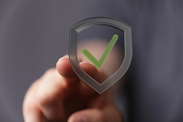 A person's hand is seen touching a digital shield with a green checkmark, symbolizing protection, security, and approval