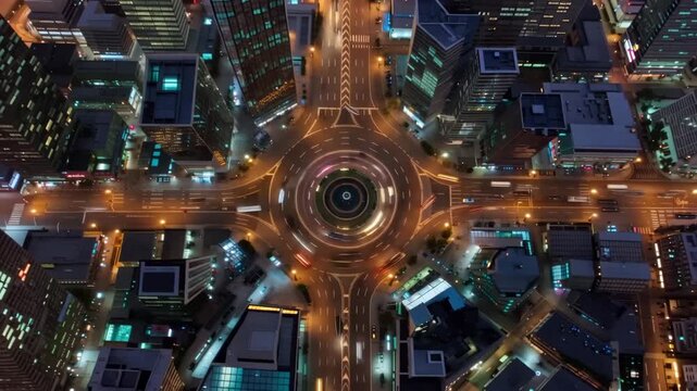 Cars move around a busy roundabout in a city at night with lights shining on the roads and buildings