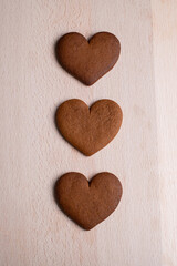 Obraz premium Three Heart-Shaped Gingerbread Cookies Arranged in a Row on a Light Wooden Surface. Top View