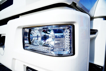 Headlight of truck close up. Close view of white truck headlight showing details of design and light features. LED headlamp, Truck headlight close-up. Bi-Xenon headlamps LED automotive lighting. © MaxSafaniuk