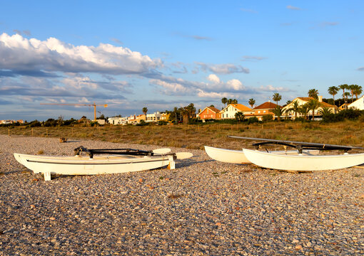 Boats on a pebble shore near houses in spain coastal. Landscape with pebble beach and white catamarans on shore. Mediterranean region of Spain near Villas and suberb houses. Almenara, Spain.