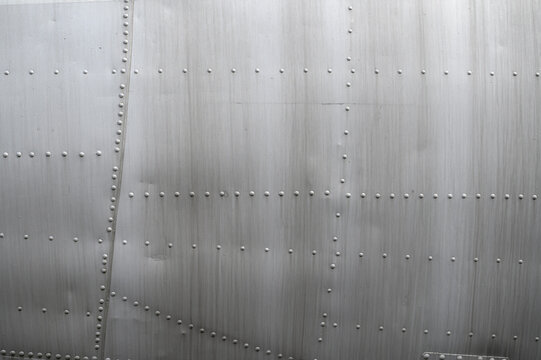 Close-up of aircraft's surface. Metal aluminum fuselage features detailed rivets, detailed view of aircraft's exterior and minimalist industrial design elements. Background, texture.