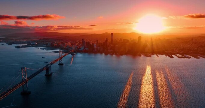 Bright setting sun over the cityscape of San Francisco, California, USA. Drone footage over the bay approaching the Oakland Bay Bridge with lively traffic.