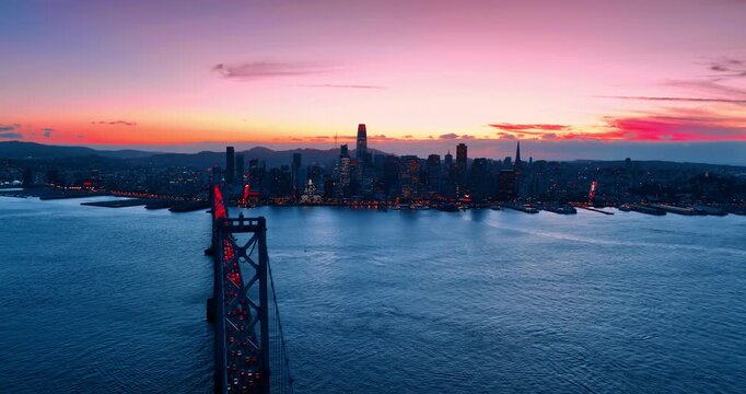 Flyover the Oakland Bay Bridge with lively hectic traffic. Approaching the skyline of San Francisco, California, USA set against pink sky at sunset.