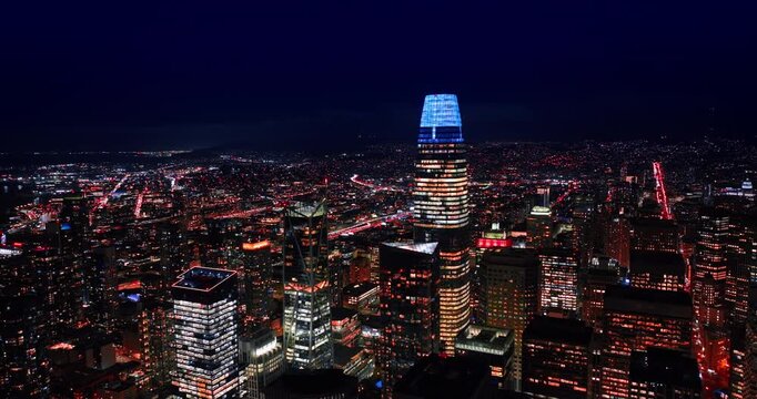 Rising over the stunning scenery of San Francisco, California, USA at night. Vast panorama of the city from drone. View on the neon top of Salesforce Tower.