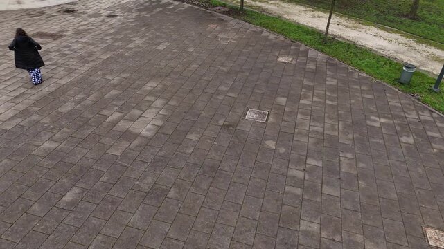 single woman walking alone across a wide stone-paved plaza, with strong negative space and minimalist composition that suggests solitude, daily life, and city atmosphere.