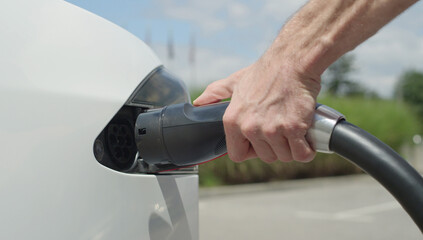 CLOSE UP: Young man charging luxury white Tesla electric car on beautiful day