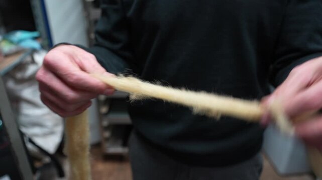 Hands of a man working with sheep wool, twisting and preparing fibers in a workshop setting with tools and materials visible