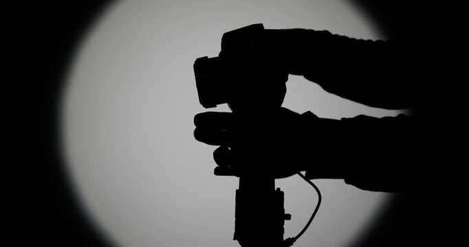 The operator sets up and connects the camera to a motorized stabilizer with a suspension, filming against a bright round light on a dark background, symbolizing film production.