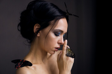 Woman with dark hair and blue eyeshadow looking down at a butterfly on her hand. Spring nature, beauty, and renewal concept. © Анна Маркина