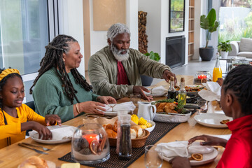 African American family passing dishes and serving roasted chicken at long wooden dining table