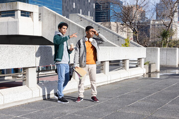 Two teenage African American males standing on plaza by concrete balustrade holding coffee, folders