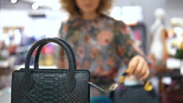 Fashionable woman browsing in a luxury boutique, comparing an exclusive snakeskin handbag with another purse in her hand, with the focus on the designer python leather accessory in the foreground