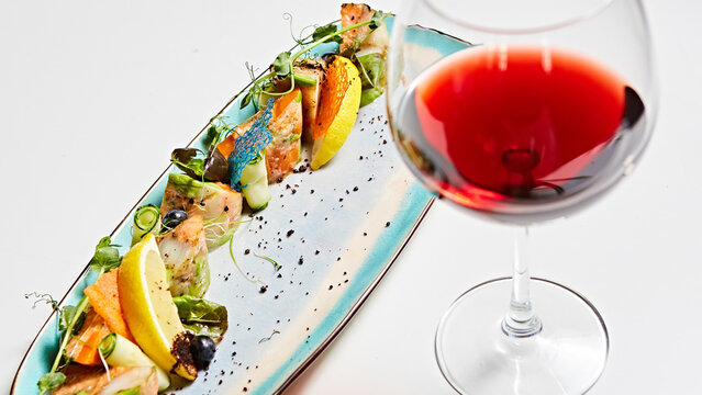 Luxury seafood appetizer paired with a glass of red wine, featuring seared fish and vibrant tuiles