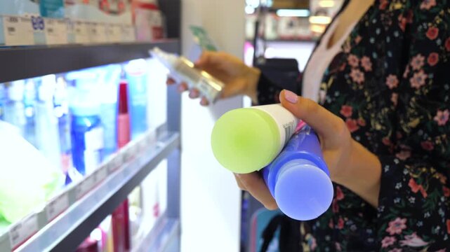 Unrecognizable woman with beautiful nails choosing between two different deodorant products at the store aisle. Close up of her hands holding cosmetics while making a purchasing decision