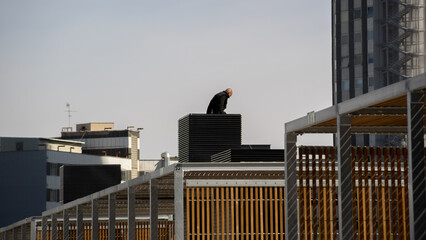Man stands on building rooftop looking out over city on a clear day with tall buildings all around © Benjamin