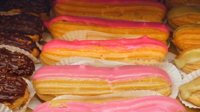 Vibrant assortment of freshly baked eclairs with colorful pink, yellow, and chocolate glazes, meticulously arranged in a bakery display case, ready for customers to enjoy a sweet treat