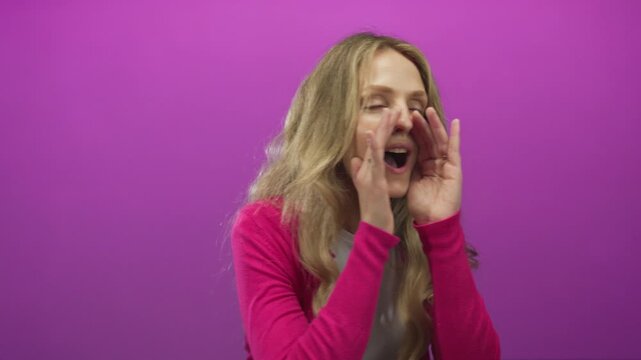Woman shouting with cupped hands against a vibrant pink background wearing a pink sweater, expressing surprise and excitement in an isolated setting.