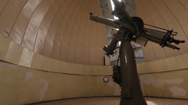 Timelapse of a large, professional telescope inside an astronomical observatory as the dome slit opens, revealing bright daylight. A scientific instrument ready for stargazing and space exploration.

