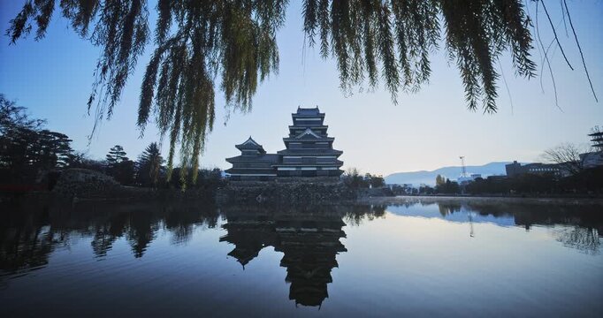 Reflection of ancient 16th century Matsumoto castle in rippling pond early in the morning