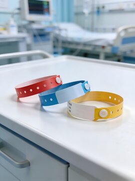 Close-up of colorful hospital patient identification wristbands on bedside table with blurred medical room background. Healthcare safety, patient tracking and hospital administration concept.