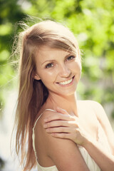 Naklejka premium A young woman with blonde hair is resting her arm on her shoulder against a softly focused green background.