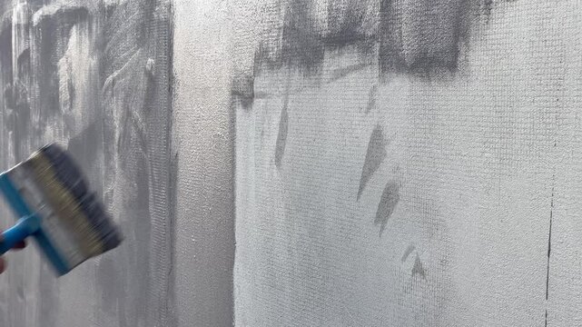 An artist paints a large canvas using a roller. The activity takes place in a studio with natural light coming in. Each frame shows different stages of painting.