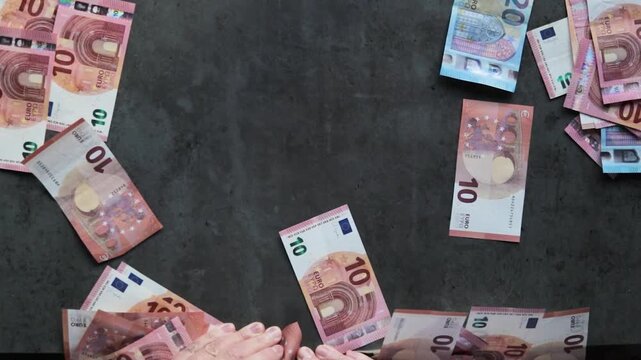 A man in a business shirt collects numerous banknotes from a table with both hands. Conceptually, this could indicate a bribe or money laundering scheme.