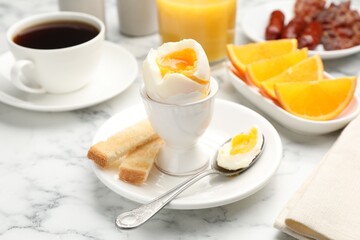 Tasty breakfast with soft boiled egg and toasted bread served on white marble table, closeup