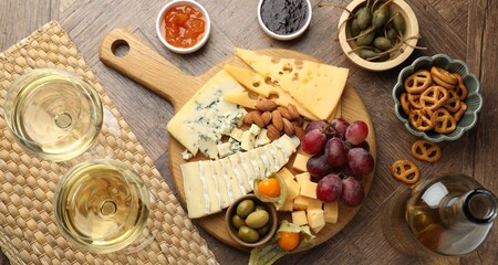 Charcuterie board with many different snacks and wine on wooden table, flat lay